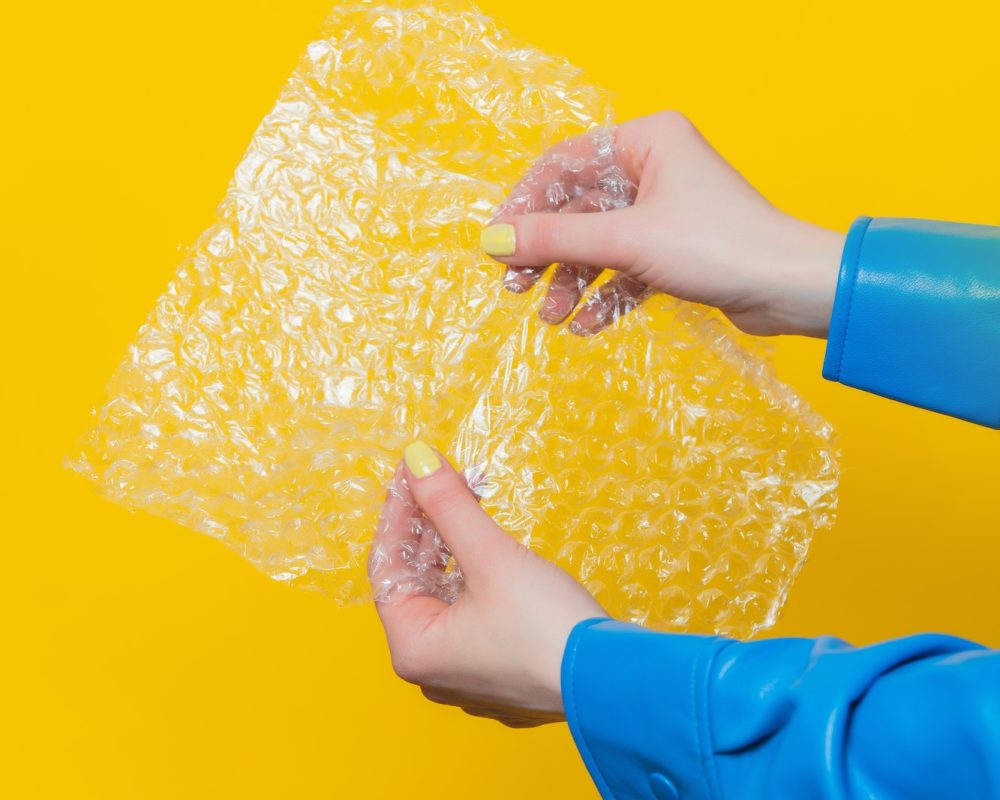female hands in blue shirt hold bubble wraps on yellow background